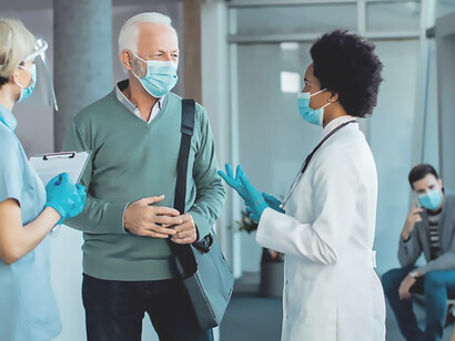Senior man with protective face mask talking to doctors at hospital hallway