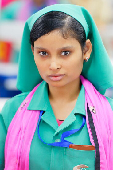 During her shift at a bustling textile factory in Jordan, a worker briefly pauses her tasks to glance at the camera, her expression reflecting both resilience and focus amidst the demanding environment