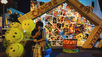 A child sits with balloons in front of a wall of movie posters, Kolkata, WB, India

