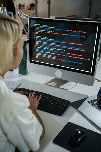 A vertical shot of a woman in an office, attentively viewing a computer screen filled with multicolored coding scripts