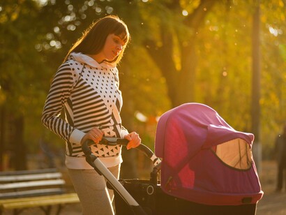 A woman pushing a stroller in a park making sure the baby doesn't feel alone
