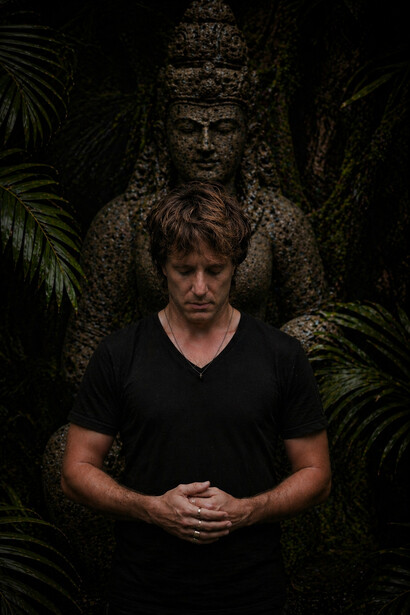 Surrounded by darkness and dense foliage, a meditative pause unfolds between the human spirit and the enduring calm of stone