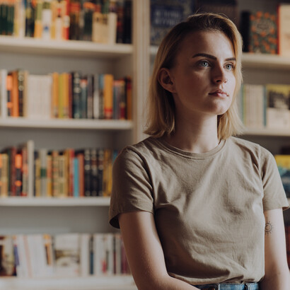 Leitora viaja nos pensamentos após pausa na leitura dentro de uma biblioteca