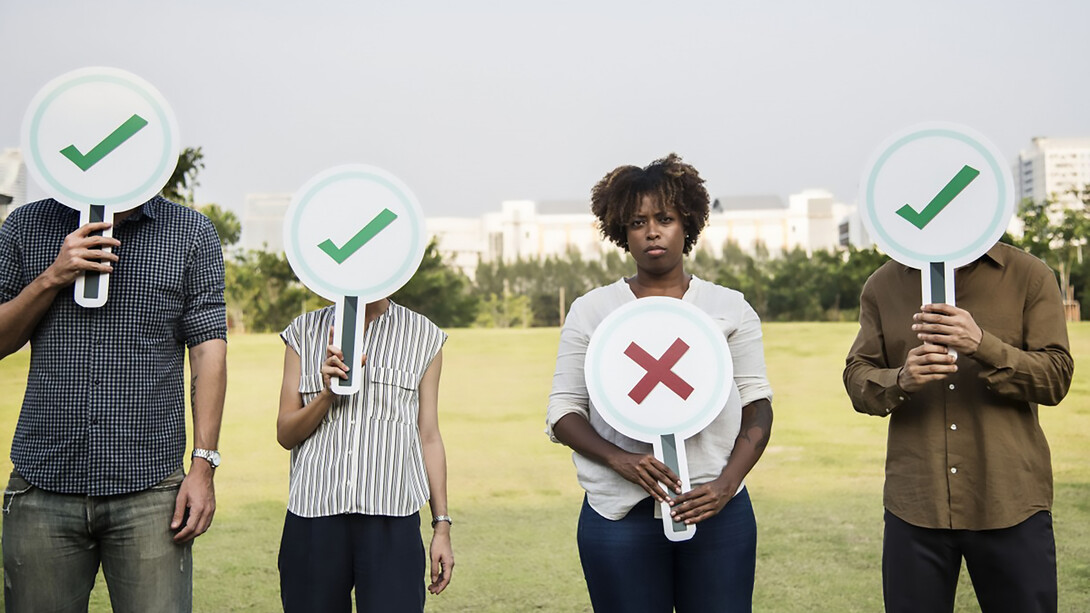 A dissatisfied Black woman gazes directly at the camera, holding a sign shaped like a cross