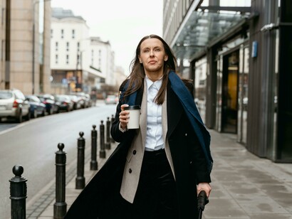 A woman wearing a black coat and scarf walks along the street