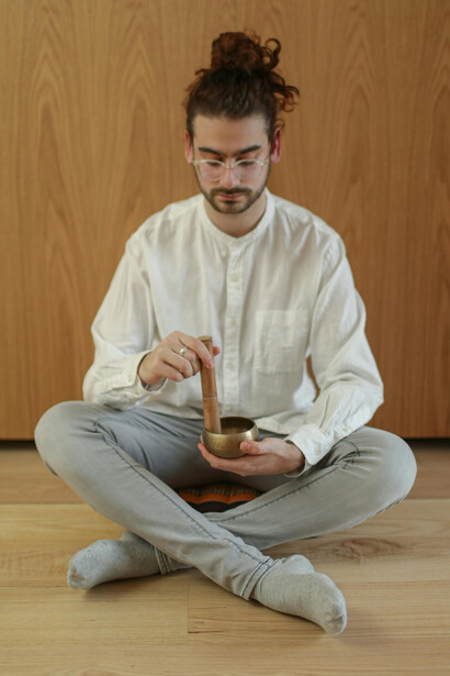 Surrounded by the soft glow of candlelight and the presence of a singing bowl, an adult man meditates indoors to cultivate relaxation, focus, and emotional balance