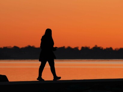 Pessoa caminhando próxima à água durante o pôr do sol. Estudos recentes associam a atividade física regular a melhores indicadores de saúde mental