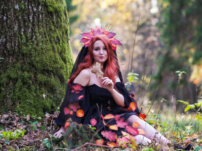 A woman wearing fantasy garments, leaning against a tree in an enchanted forest