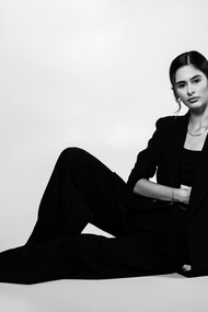A portrait of a female model posing confidently in a studio, dressed in a sleek black suit that embodies modern sophistication and timeless style