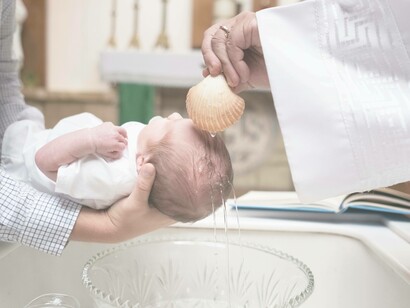 A priest performs the religious pouring of water on the baby's head during his baptism as the godfather watches on