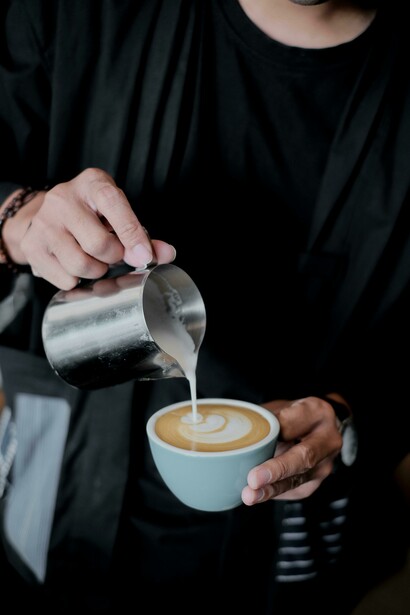 A person pours milk into a freshly brewed coffee at a startup café