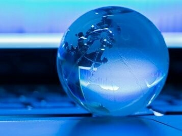 A transparent glass globe placed on a laptop keyboard, a visual representation of the Princonser method's approach to business law, where universal principles guide the evolution of legal systems in response to global economic and technological changes