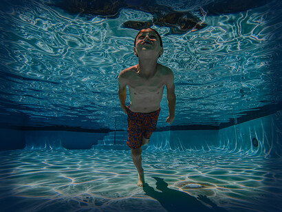 The boy swims up to the surface of the swimming pool