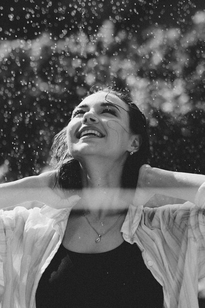 A grayscale image capturing a woman laughing with happiness while rain falls around her