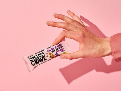 An organic low-sugar granola and muesli bar from The Organic Crave Company, presented on a table with a close-up view highlighting its ingredients