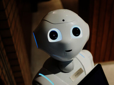 A white robot toy holding a black tablet, symbolizing AI companionship, virtual friendships, and robotic therapy