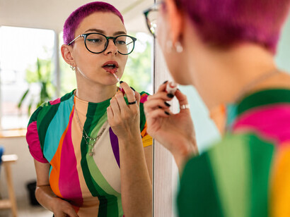 Young woman with dyed pink hair applying makeup in front of a mirror