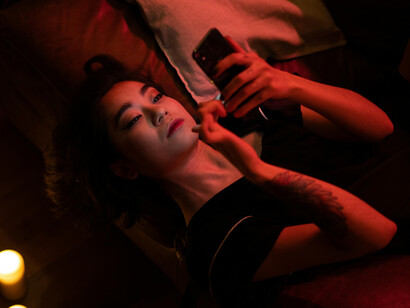 Woman in bed on her phone, reflecting digital loneliness, the millennial loneliness aesthetic, and the isolation of modern life