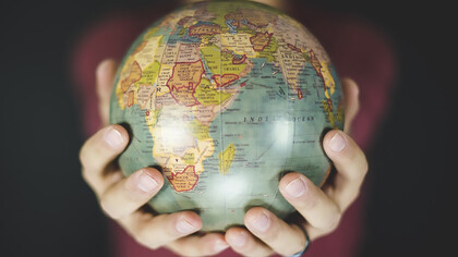A person gently cradles a small globe in both hands, symbolizing a deep connection to the world and a commitment to global awareness and cultural understanding