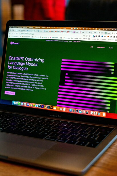 The open MacBook features a sleek design, its screen displaying the homepage of ChatGPT, an advanced AI language model designed to facilitate dynamic communication and provide users with relevant information