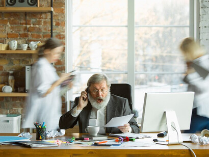 The weary boss, overwhelmed at his desk, is surrounded by blurred coworkers, reflecting the ongoing stress, workplace anxiety, and growing discontent among the team