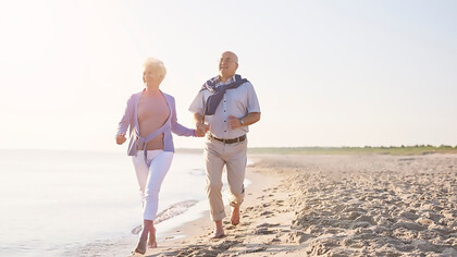 A senior couple enjoys their summer vacation, running along the beach together