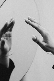 A person delicately reaches out to touch a mirror, and in this interaction, a reflection of her hand appears over the mirror's surface, creating an intriguing visual connection between reality and its mirrored counterpart 