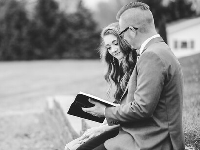 A greyscale image of a man and woman in formal attire, reading together in a garden