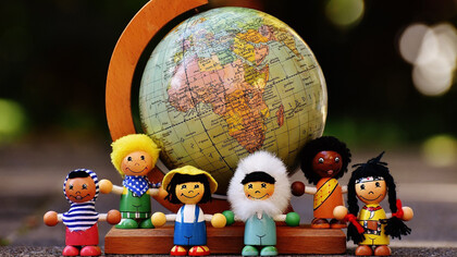 Figures of children in the shapes of different nationalities in front of the world globe
