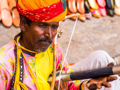 A man is sitting on the ground, playing a musical instrument, India