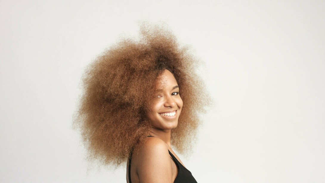 A woman with voluminous hair smiling, showcasing the beauty of natural texture and self-love—celebrating the uniqueness of coily and texturized hair