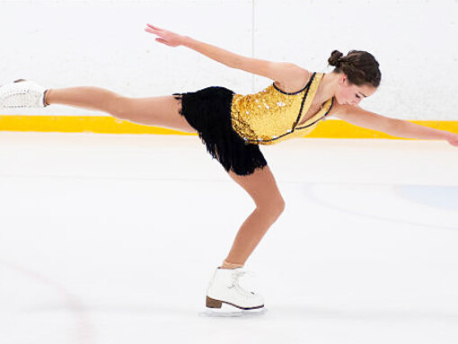 A girl figure skating on smooth white ice, elegantly dressed in her costume
