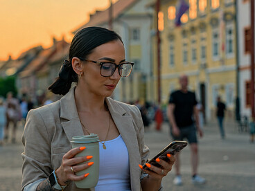 Businesswoman walking through the streets of Ljubljana, Slovenia, while using her smartphone and drinking coffee