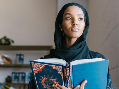 A woman wearing a hijab holds a copy of the Quran