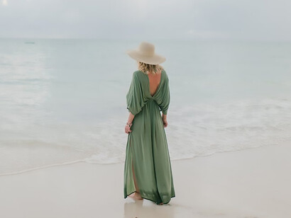 As the wind whips through the air, a woman gracefully walks along the damp sandy beach, the rhythmic sound of crashing waves providing a serene soundtrack to her contemplative journey