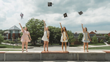 Four students throw their caps into the air to celebrate their graduation