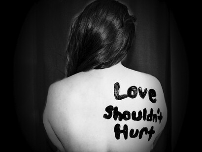 Una mujer con un mensaje pintado en su espalda que reza "El amor no debería doler". La violencia en la pareja es una de las formas más comunes de violencia de género