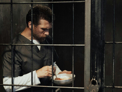A solitary man peers out from his cell, framed by bars