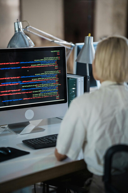Vertical shot of a woman in an office, focused on a computer screen displaying multicolored code