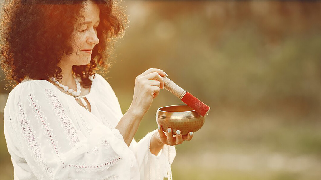 A woman holding a chanting bowl in a natural setting, embodying Ayurveda and a healthy lifestyle