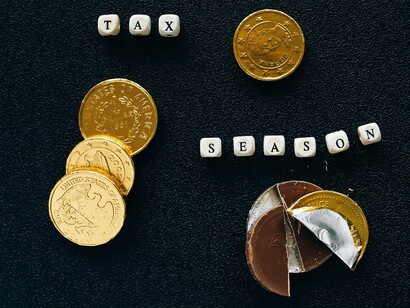 Coins arranged beneath the words “tax season,” representing the growing financial strain of modern economic policy