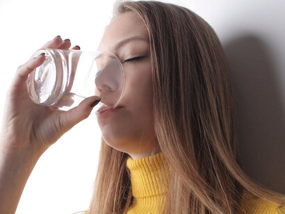 A woman in a vibrant yellow t-shirt staying hydrated by drinking water, promoting good health and preventing dehydration