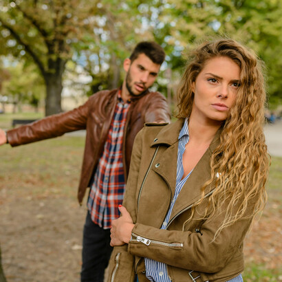 A couple in brown jackets stand apart near a tree, symbolizing emotional distance and loneliness in their relationship