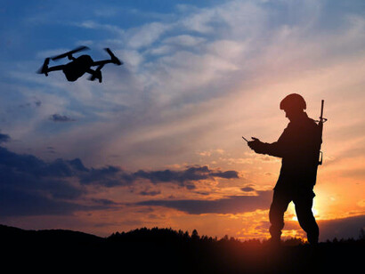The dark outline of a soldier controlling a drone and monitoring data on a laptop during a military operation