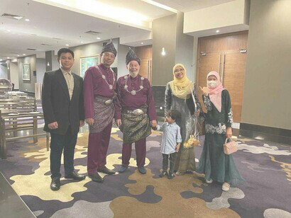 Professor Jeffrey Levett with a colleague and his family posing outside the banquet hall of the Eurasian Bridges for Peace ceremony in Malaysia