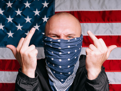 A bald man with half his face covered flips his middle finger in defiance