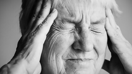 Elderly woman experiencing a stroke, holding her head in pain