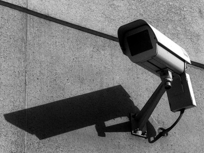 Una cámara de vigilancia observa desde lo alto mientras su sombra se proyecta sobre el muro