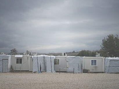 A white and gray camper trailer stands on a green grass field under a gray cloudy sky during daytime, evoking a sense of transience and movement, reminiscent of the journey of migration