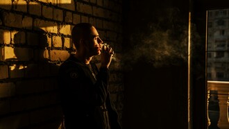 A man leaning against a wall smoking a cigarette 